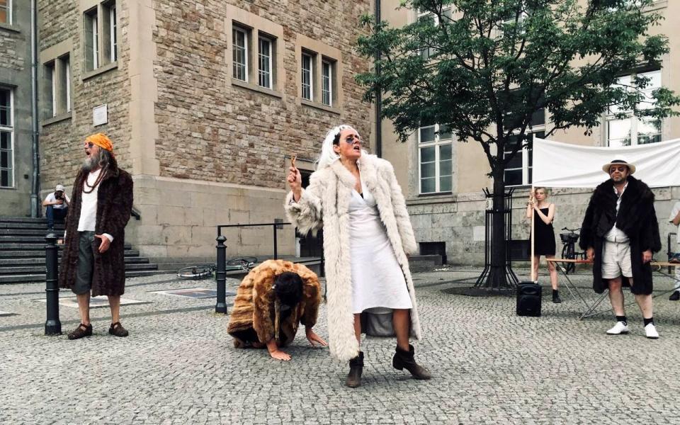 Vier Schauspieler in Pelzmänteln schreien auf einem Platz